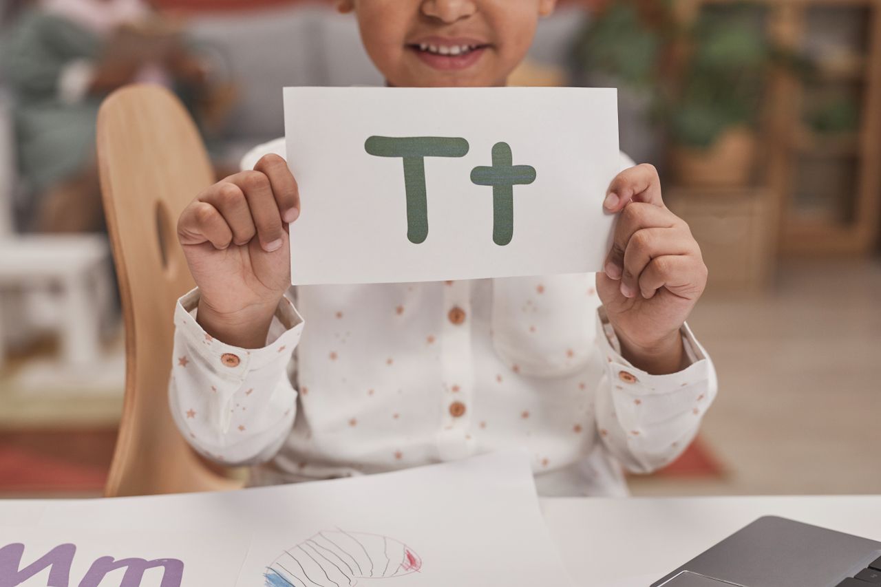 The Art of Drawing Readers In: Your attractive post title goes here Close-up of child holding card with letter T in classroom, encouraging early education.