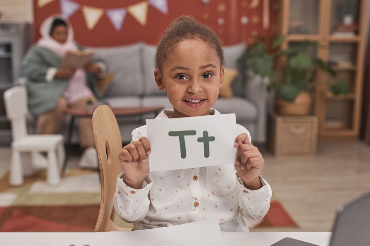 Home A cheerful child holds an alphabet card in a cozy indoor setting, engaging in educational play.