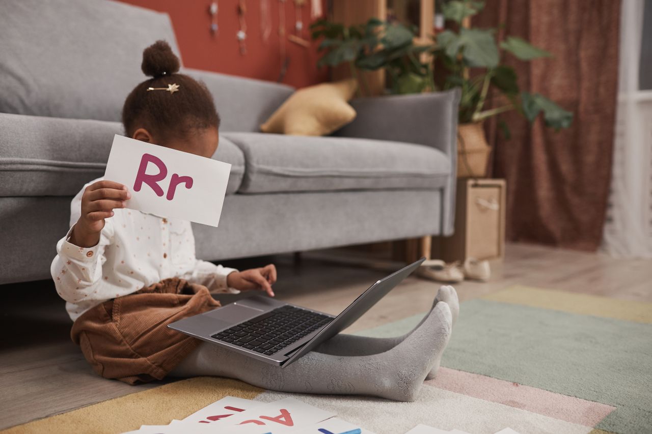 Home Child learning with alphabet cards and laptop at home, embracing online education.