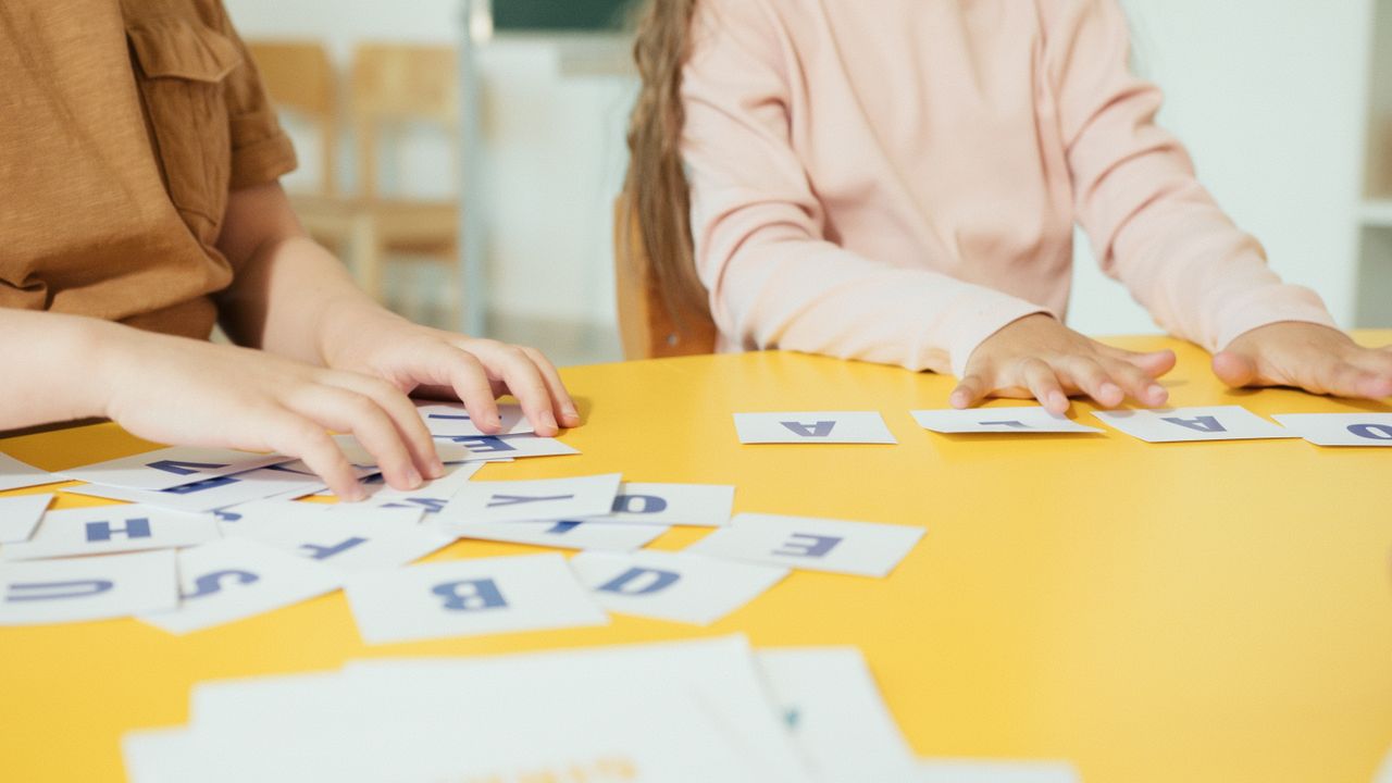 Crafting Captivating Headlines: Your awesome post title goes here Children arranging alphabet cards on a yellow table in a classroom setting.